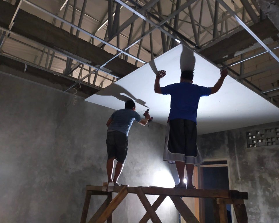 Dua tukang memasang lembaran plafon gypsum pada pekerjaan renovasi